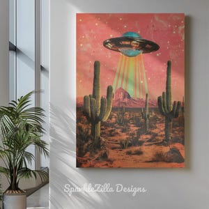May include: A canvas print depicts a desert scene with cacti and a mountain range under a pink sky. A retro-style UFO hovers above, emitting a beam of light. The artwork is signed "SparkleZilla Designs".