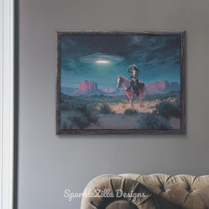 May include: Framed art print showing a cowboy on horseback looking at a UFO above a desert scene. The artwork features a night sky with stars and a glowing spacecraft. The print is in a rustic wooden frame.
