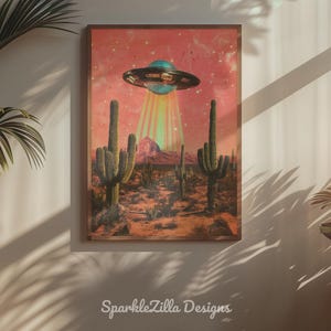 Könnte beinhalten: Gerahmter Kunstdruck mit einer Wüstenlandschaft mit Kakteen und einer Bergkette unter einem rosa Himmel. Eine türkis-silberne UFO schwebt darüber und strahlt einen Lichtstrahl aus. Der Text "SparkleZilla Designs" befindet sich unten.