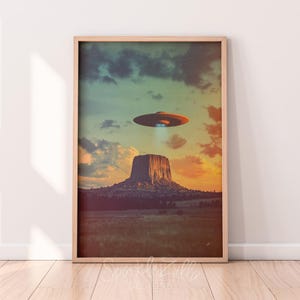 Könnte beinhalten: Ein digitaler Kunstdruck mit einer großen Felsformation in einer Wüstenlandschaft, über der eine fliegende Untertasse schwebt. Der Himmel ist ein Farbverlauf von Blau, Grün und Orange.