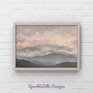 Könnte beinhalten: Ein gerahmter Kunstdruck mit einer Berglandschaft unter einem bewölkten Himmel. Das Kunstwerk hat eine weiche, gedämpfte Farbpalette mit Grautönen, Rosa und Beige. Der Rahmen ist hellrosa. Der Text "SparkleZilla Designs" befindet sich unten.