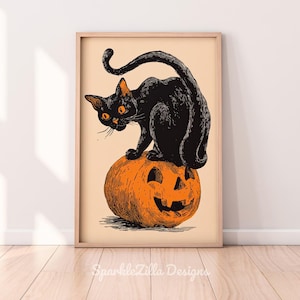 Puede incluir: Un estampado enmarcado de Halloween de estilo vintage con un gato negro con ojos naranjas posado sobre una calabaza naranja. El estampado tiene un fondo beige y un marco de madera. El texto "SparkleZilla Designs" está en la parte inferior.