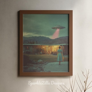 May include: Framed print featuring a retro-style scene of a woman in a dress standing in front of a mid-century modern house. An unidentified flying object shines a pink beam of light. The print is framed in a brown wooden frame. The text "SparkleZilla Designs" is at the bottom.
