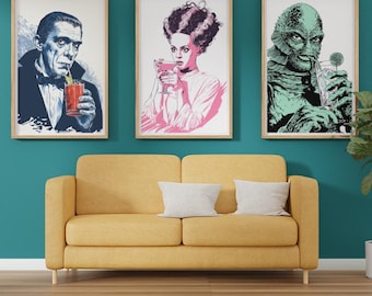 May include: Three framed art prints featuring classic movie monsters: Dracula, the Bride of Frankenstein, and the Creature from the Black Lagoon, each enjoying a cocktail. The prints are displayed above a yellow sofa against a teal wall. The artist's name, SparkleZilla Designs, is at the bottom.