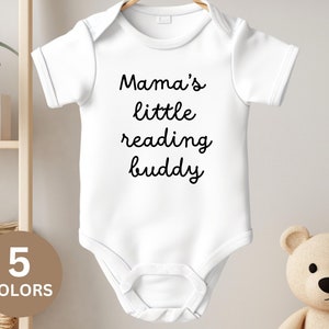 Pode incluir: Macacão branco para bebê com texto preto que diz "Mama's little reading buddy".