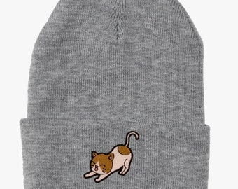 Puede incluir: Gorro de punto gris con un pequeño gato de dibujos animados bordado en la parte delantera. El gato es marrón, blanco y rosa.