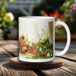 May include: White ceramic mug with a brown bear sleeping in a forest scene with red strawberries and green leaves.