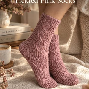 Może przedstawiać: Para dzianinowych skarpet w kolorze przybrudzonego różu z teksturowanym wzorem warkoczowym. U góry widnieje napis KNITTING PATTERN Tickled Pink Socks. Skarpety mają ściągacz oraz wyprofilowaną piętę, ukazującą szczegółowy splot przędzy.