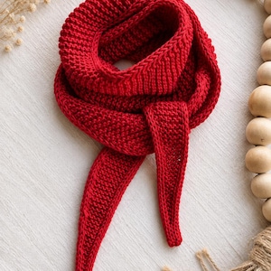May include: A vibrant red knitted scarf featuring a textured garter stitch pattern. The scarf is designed with a tapered, pointed end and is looped to create a circular shape, showcasing the consistent yarn density and deep crimson color throughout.