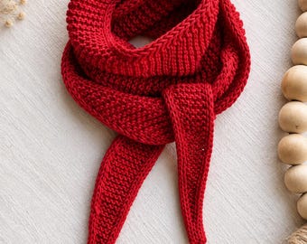 May include: A vibrant red knitted scarf featuring a textured garter stitch pattern. The scarf is designed with a tapered, pointed end and is looped to create a circular shape, showcasing the consistent yarn density and deep crimson color throughout.