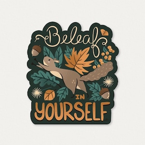 May include: A die-cut sticker featuring a brown squirrel leaping among orange and green autumn leaves, acorns, and berries. The text "Beleaf IN YOURSELF" is written in a decorative script and bold block font against a dark green background.