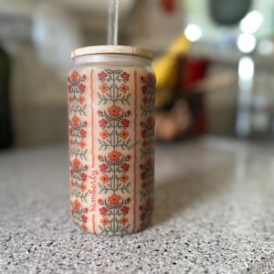 Pu&ograve; includere: Un bicchiere di vetro riutilizzabile con un motivo floreale e la parola "Kimberly" stampata sul lato. Il bicchiere ha un coperchio in legno e una cannuccia.