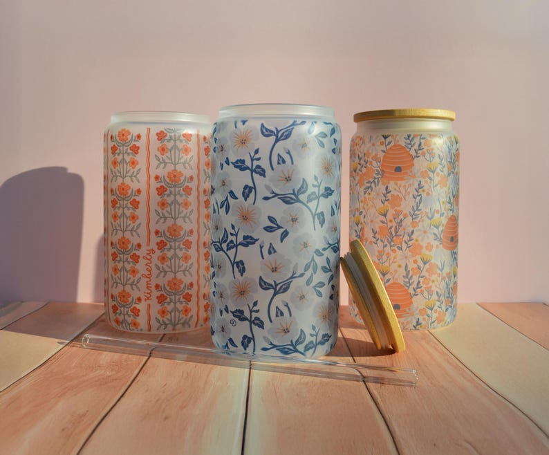 Pu&ograve; includere: Tre bicchieri di vetro smerigliato con diversi motivi floreali. I bicchieri sono su una superficie di legno. Il bicchiere a sinistra ha un motivo floreale rosso e arancione, il bicchiere al centro ha un motivo floreale blu e bianco, e il bicchiere a destra ha un motivo floreale giallo e arancione con un design a nido d'ape.