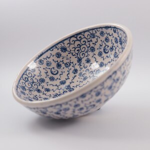 Puede incluir: Un cuenco de cer&aacute;mica blanca con un patr&oacute;n floral azul y blanco. El cuenco est&aacute; ligeramente inclinado y el interior es visible.