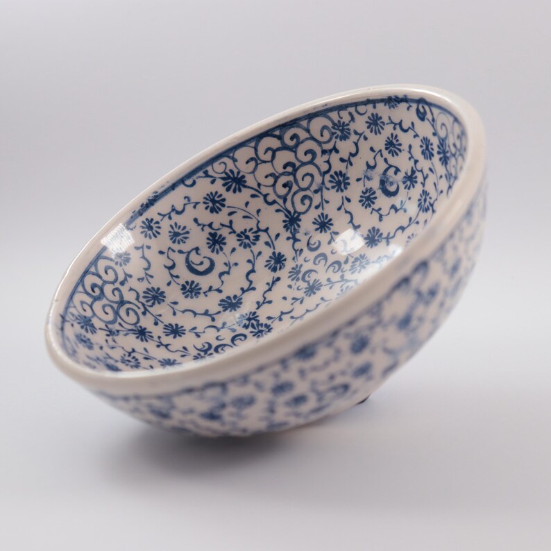 Puede incluir: Un cuenco de cer&aacute;mica blanca con un patr&oacute;n floral azul y blanco. El cuenco est&aacute; ligeramente inclinado y el interior es visible.