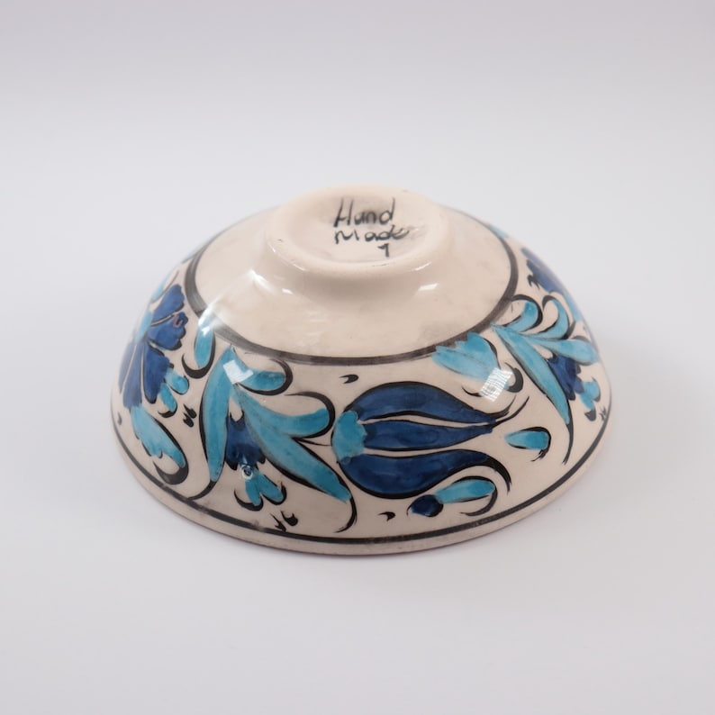 Puede incluir: Un cuenco de cer&aacute;mica blanca con un dise&ntilde;o floral azul y turquesa. El cuenco est&aacute; pintado a mano y dice "Hand Made" en la parte inferior.