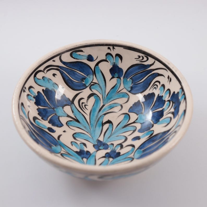 Puede incluir: Un cuenco de cer&aacute;mica blanca con un dise&ntilde;o floral azul y turquesa. El cuenco est&aacute; pintado a mano con detalles intrincados y presenta un patr&oacute;n turco tradicional.