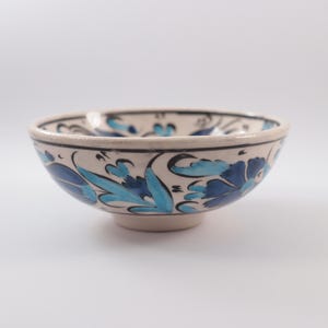 Puede incluir: Un peque&ntilde;o cuenco de cer&aacute;mica blanca con un dise&ntilde;o floral azul y turquesa. El cuenco tiene una forma redondeada y un peque&ntilde;o pie.