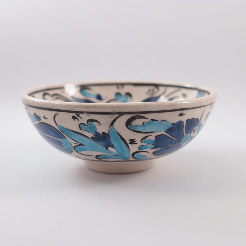 Puede incluir: Un peque&ntilde;o cuenco de cer&aacute;mica blanca con un dise&ntilde;o floral azul y turquesa. El cuenco tiene una forma redondeada y un peque&ntilde;o pie.