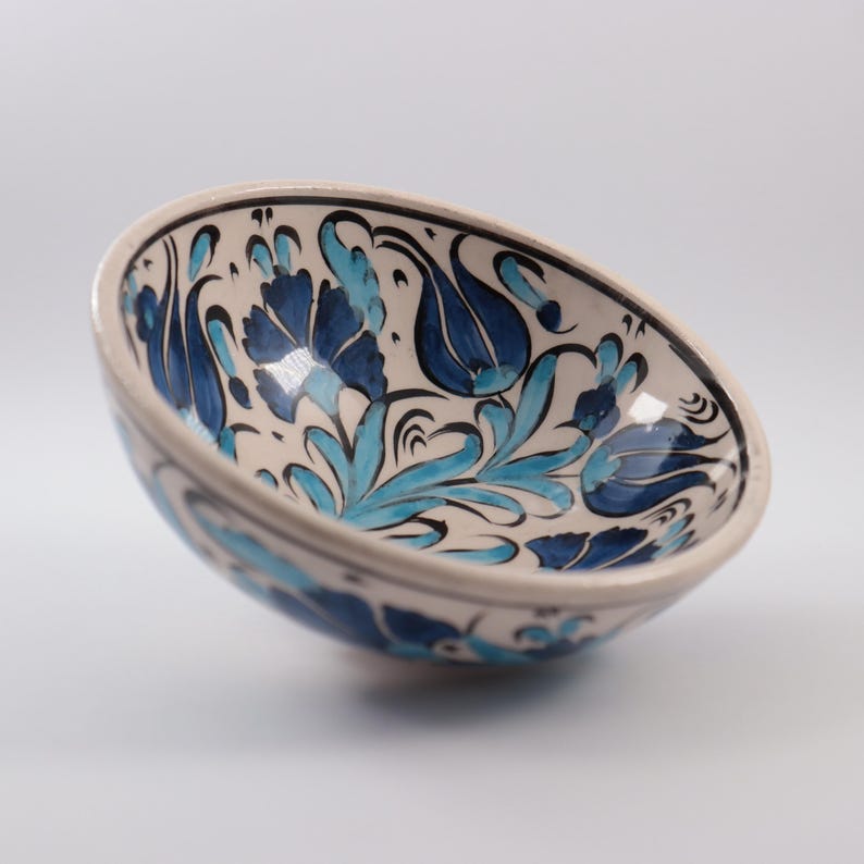 Puede incluir: Un cuenco de cer&aacute;mica blanca con un dise&ntilde;o floral azul y turquesa. El cuenco est&aacute; pintado a mano con detalles intrincados y es perfecto para servir aperitivos o postres.