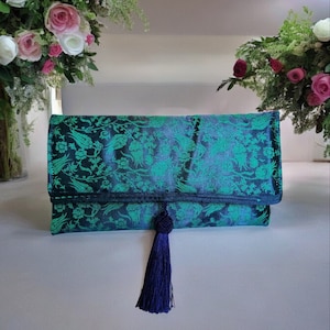 May include: A teal blue clutch bag with a floral pattern and a dark blue tassel.