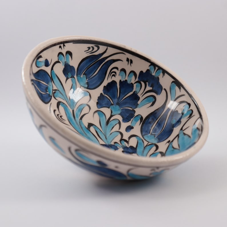 Puede incluir: Un cuenco de cer&aacute;mica blanca con un dise&ntilde;o floral azul y turquesa. El cuenco est&aacute; pintado a mano con detalles intrincados y presenta un patr&oacute;n turco tradicional.