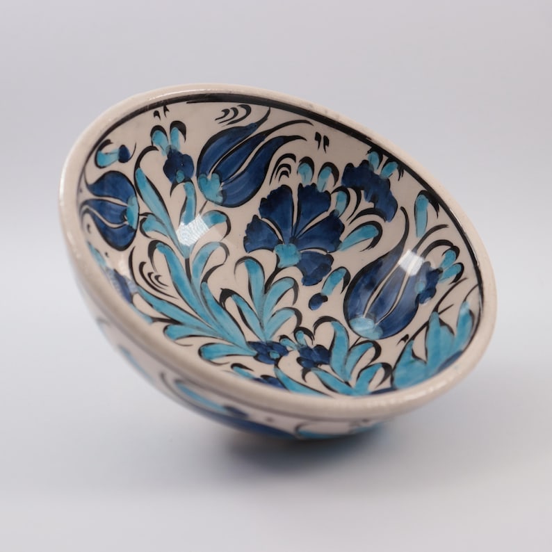 Puede incluir: Un cuenco de cer&aacute;mica blanca con un dise&ntilde;o floral azul y turquesa. El cuenco est&aacute; decorado con tulipanes y hojas estilizadas.