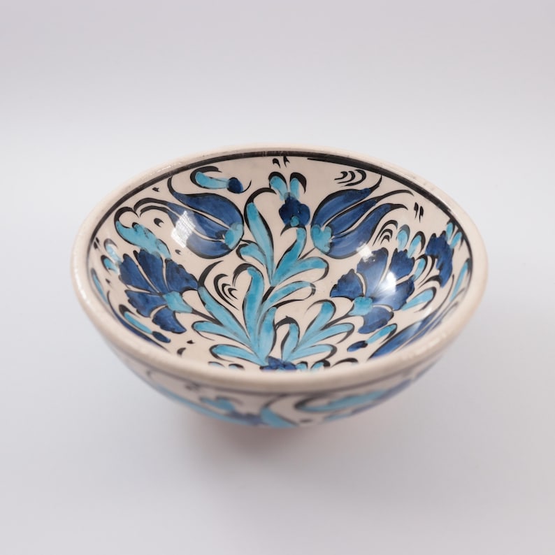 Puede incluir: Un cuenco de cer&aacute;mica blanca con un dise&ntilde;o floral azul y blanco. El cuenco est&aacute; decorado con flores y hojas estilizadas.