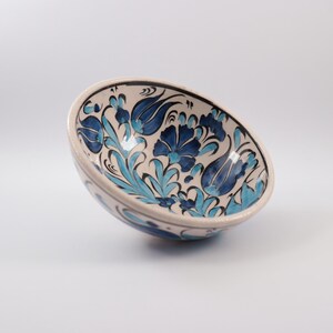 Puede incluir: Un cuenco de cer&aacute;mica blanca con un dise&ntilde;o floral azul y turquesa. El cuenco est&aacute; pintado a mano con detalles intrincados y es perfecto para servir aperitivos o postres.