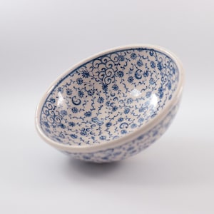 Könnte beinhalten: Eine weiße Keramikschüssel mit einem blauen und weißen Blumenmuster. Die Schüssel ist leer und steht auf einer weißen Oberfläche.