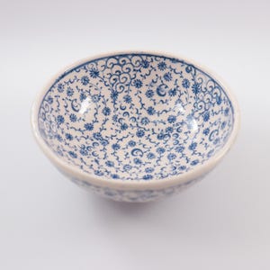 Puede incluir: Un taz&oacute;n de cer&aacute;mica blanco con un patr&oacute;n floral azul y blanco. El taz&oacute;n es redondo y tiene un borde ligeramente curvado.