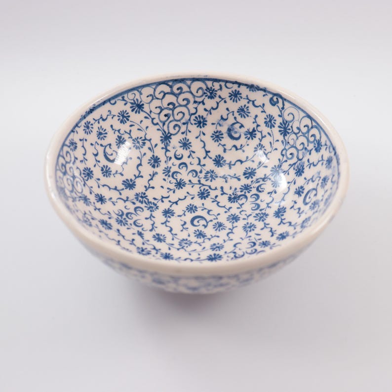 Puede incluir: Un taz&oacute;n de cer&aacute;mica blanco con un patr&oacute;n floral azul y blanco. El taz&oacute;n es redondo y tiene un borde ligeramente curvado.