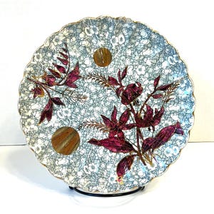 May include: A vintage ceramic plate with a scalloped edge and a blue and white crackle glaze. The plate features a floral design with pink flowers and gold accents.
