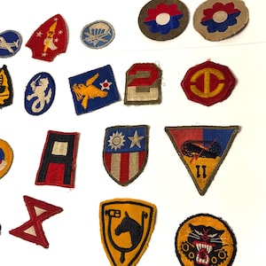 May include: A collection of vintage military patches in various shapes and colors. The patches feature emblems such as a horse head, a tiger, and a parachute. Some patches have the number "2" or the number "11".