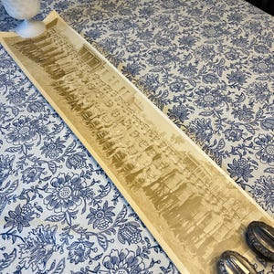 May include: A sepia-toned photograph of a large group of people standing in a line. The people are all dressed in formal attire and appear to be from the early 1900s. The photograph is on a white tablecloth with a blue floral pattern.