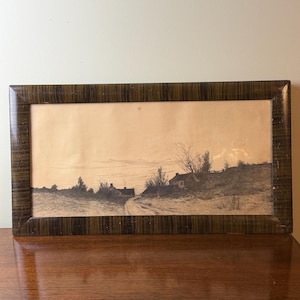May include: A rectangular framed landscape print featuring a monochromatic sketch of a rural path leading toward small houses and bare trees. The artwork is enclosed in a dark, vertically textured wooden frame with a polished, glossy finish.