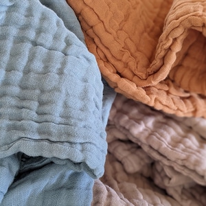 May include: A stack of three soft, textured fabric blankets in blue, orange, and beige.