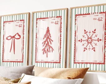 Puede incluir: Tres impresiones artísticas enmarcadas con temática navideña. Cada impresión presenta un diseño rojo sobre un fondo crema, incluyendo un lazo, un árbol y un copo de nieve. Los marcos tienen un acabado de madera clara y están sobre un fondo a rayas verdes y blancas.