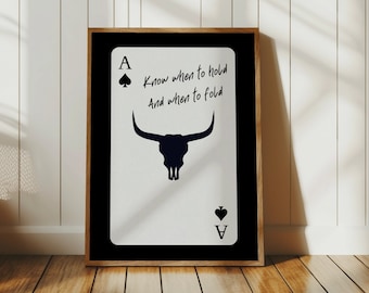 May include: Framed art print featuring an Ace of Spades card design. The card displays a black bull skull silhouette and the text "Know when to hold and when to fold." The artwork is set against a white background with a black border and a wooden frame.