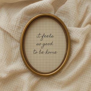 it feels so good to be home quote in hand drawn script typography on neutral beige gingham background in a vintage oval frame.