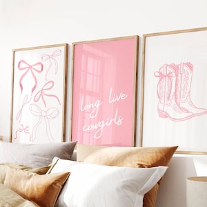 Puede incluir: Tres impresiones enmarcadas de color rosa con texto blanco e ilustraciones. La impresión de la izquierda presenta lazos rosas. La impresión del medio dice "long live cowgirls". La impresión de la derecha muestra un par de botas de vaquero rosas.