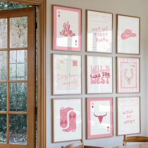 May include: A collection of framed art prints with a Western theme. The prints feature pink and white designs, including a cactus, cowboy hat, horseshoe, and the phrases "Wild Like the West" and "Not My First Rodeo."