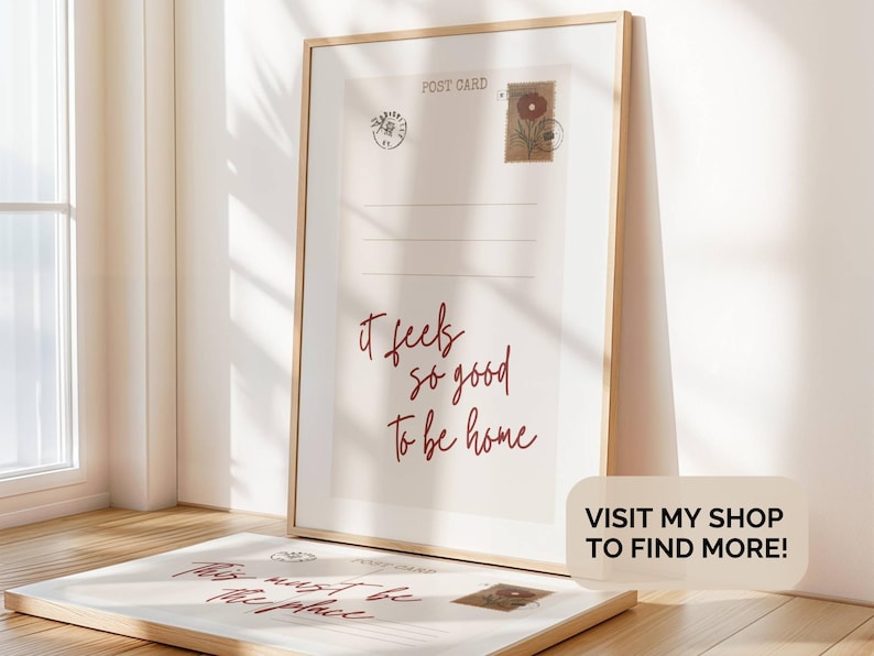 Pu&ograve; includere: Una stampa incorniciata con un design di cartolina vintage che presenta il testo "It feels so good to be home". La stampa &egrave; in una cornice di legno chiaro e ha uno sfondo bianco con testo rosso.