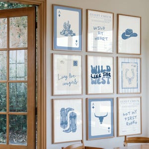 May include: A collection of framed art prints with a Western theme. The prints feature blue and white illustrations of a cactus, cowboy hat, horseshoe, and playing cards. Text includes "Wild at Heart", "Long live cowgirls", and "Wild like the West".