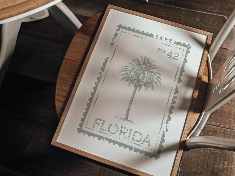 May include: A framed print featuring a palm tree design within a postage stamp border. The print is in shades of green and white, with the word "FLORIDA" and "USA 42" visible. The frame is made of wood.