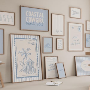 May include: A display of framed art prints with a coastal theme. The prints feature beach-related imagery and text, including phrases like "Coastal Cowgirl Beach Club" and "Meet me at the beach." The colour palette is primarily blue and beige.