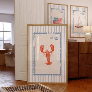 May include: Three framed nautical-themed prints. The largest features a red lobster illustration with "USA 42" text. The other two prints display a sailboat and an American flag, also with "USA 42" text. All are framed in light wood.