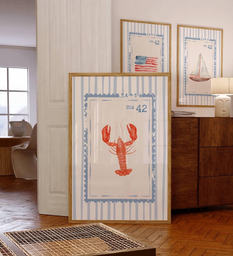 May include: Three framed nautical-themed prints. The largest features a red lobster illustration with "USA 42" text. The other two prints display a sailboat and an American flag, also with "USA 42" text. All are framed in light wood.