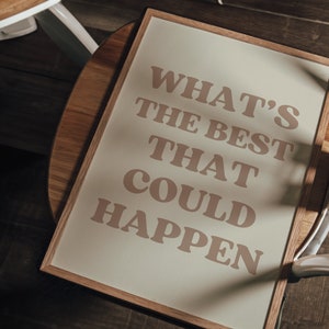 May include: A framed print with the text "What's the best that could happen" in a light brown colour on a cream background.