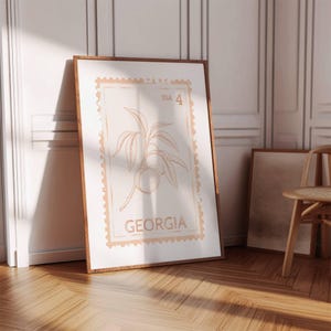 Puede incluir: Un estampado enmarcado con un diseño de rama de melocotón al estilo de un sello postal. La impresión es de color melocotón cálido con el texto "USA 4" y "GEORGIA". El marco es de color madera oscura.